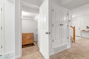 Hallway with light tile patterned floors, light colored carpet, and stairway