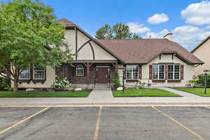 Tudor home featuring stucco siding, roof with shingles, a chimney, and uncovered parking