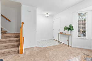 Entrance foyer featuring ornamental molding, light colored carpet, stairs, a textured ceiling, and light tile patterned flooring