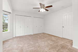 Unfurnished bedroom with two closets, light carpet, and a ceiling fan