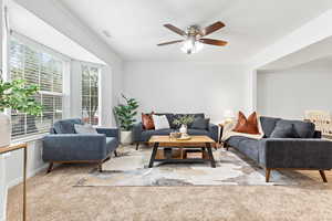 Living room featuring light carpet, ornamental molding, a textured ceiling, and ceiling fan