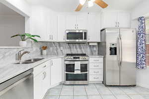 Kitchen featuring appliances with stainless steel finishes, white cabinets, light stone counters, decorative backsplash, and light tile patterned floors