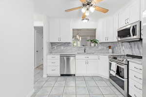 Kitchen with appliances with stainless steel finishes, light tile patterned floors, and white cabinets