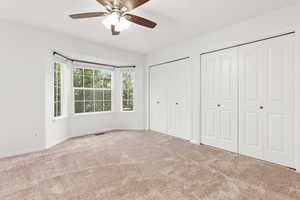 Unfurnished bedroom with two closets, carpet, and a ceiling fan