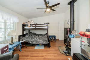 Bedroom with a wood stove, lofted ceiling, light wood-type flooring, and ceiling fan