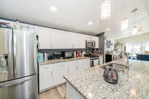 Kitchen featuring stainless steel appliances, white cabinetry, light stone counters, hanging light fixtures, and recessed lighting