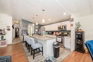 Kitchen featuring a kitchen breakfast bar, appliances with stainless steel finishes, hanging light fixtures, a kitchen island with sink, and vaulted ceiling