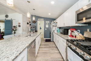 Kitchen featuring a barn door, stainless steel appliances, white cabinetry, and recessed lighting