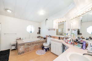 Full bath featuring a garden tub, light wood-style floors, double vanity, and a shower stall