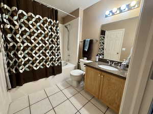 Full bathroom featuring light tile patterned flooring, shower / bath combination with curtain, a textured ceiling, and vanity