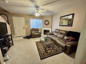 Living area featuring a textured ceiling, light colored carpet, a glass covered fireplace, a ceiling fan, and light tile patterned floors