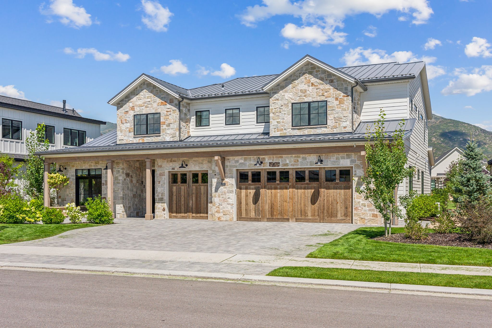 View of front facade with a standing seam roof, stone siding, a metal roof, and an attached garage