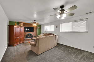 Living room featuring a fireplace, dark carpet, a textured ceiling, and a ceiling fan