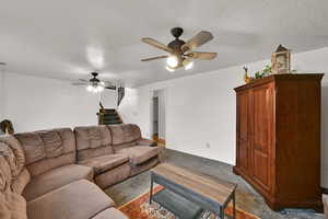 Carpeted living area with a textured ceiling, stairway, and a ceiling fan