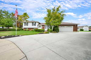 Split level home with brick siding, concrete driveway, a front yard, and an attached garage