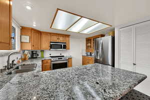 Kitchen featuring light stone countertops, decorative backsplash, stainless steel appliances, glass insert cabinets, and a peninsula