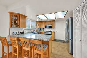 Kitchen featuring a peninsula, light stone counters, a kitchen breakfast bar, tasteful backsplash, and glass insert cabinets