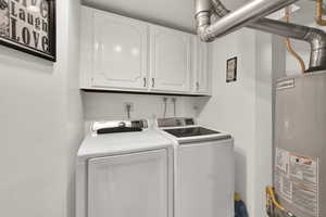 Washroom featuring water heater, cabinet space, and washing machine and dryer