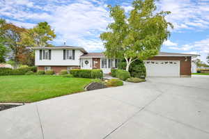 Tri-level home featuring driveway, brick siding, a front lawn, and an attached garage
