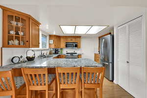 Kitchen featuring stainless steel appliances, tasteful backsplash, a peninsula, a kitchen breakfast bar, and light stone countertops