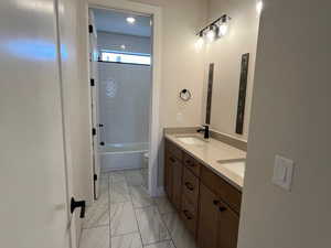 Bathroom featuring shower / washtub combination, double vanity, and light marble finish flooring