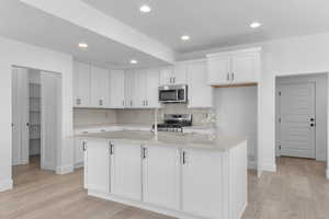 Kitchen with white cabinets, tasteful backsplash, light wood-type flooring, recessed lighting, and stainless steel appliances