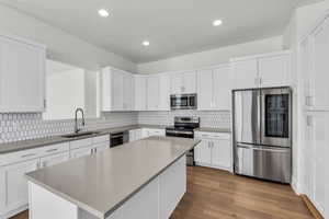 Kitchen featuring appliances with stainless steel finishes, white cabinets, dark wood finished floors, a center island, and recessed lighting