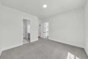 Unfurnished bedroom with a spacious closet, light carpet, and ensuite bath