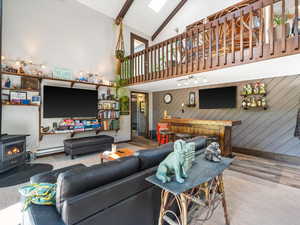 Living area featuring high vaulted ceiling, a wood stove, wood finished floors, beam ceiling, and a baseboard radiator