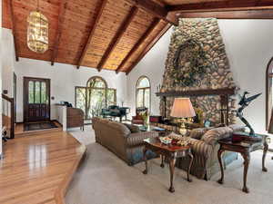 Living area featuring high vaulted ceiling, a wood ceiling with exposed beams, light wood-style floors, a chandelier, and a stone fireplace