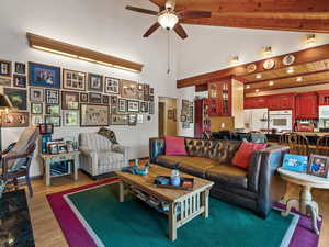 Living room featuring high vaulted ceiling, light wood-type flooring, a wooden ceiling with exposed beams, and a ceiling fan