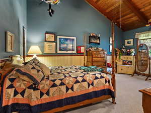 Carpeted bedroom with a wooden ceiling with exposed beams, high vaulted ceiling, and wainscoting