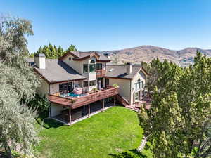 Rear view of house with a chimney, a deck with mountain view, stucco siding, stairway, and a yard