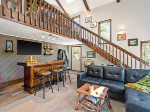 Living area with high vaulted ceiling, beam ceiling, a bar, wood finished floors, and stairs