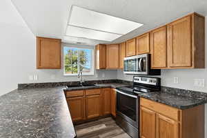 Kitchen featuring stainless steel appliances, brown cabinets, dark wood-style floors, and a textured ceiling