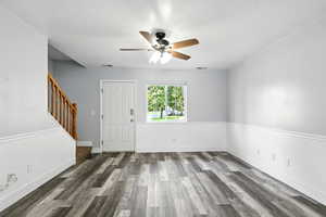 Unfurnished living room with dark wood-type flooring, stairway, and a ceiling fan