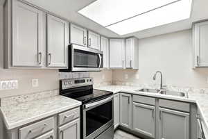 Kitchen with gray cabinetry, appliances with stainless steel finishes, and light stone counters