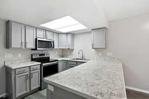 Kitchen with gray cabinetry, stainless steel appliances, light countertops, a peninsula, and dark wood finished floors