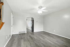 Spare room with arched walkways, dark wood-type flooring, and a ceiling fan