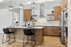 Kitchen featuring a breakfast bar area, brown cabinets, decorative backsplash, and wall chimney exhaust hood