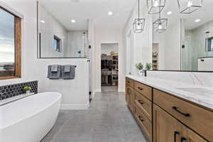 Bathroom featuring a walk in closet, a shower stall, double vanity, a soaking tub, and recessed lighting