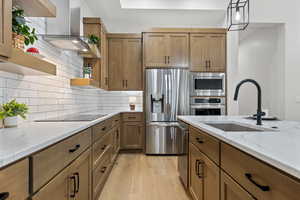 Kitchen with decorative backsplash, open shelves, appliances with stainless steel finishes, brown cabinets, and light wood finished floors