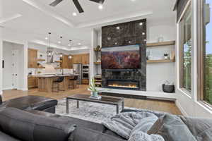 Living room featuring a premium fireplace, light wood-style flooring, a tray ceiling, ceiling fan, and recessed lighting