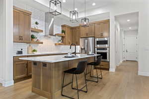 Kitchen with brown cabinetry, decorative light fixtures, open shelves, a kitchen island with sink, and recessed lighting