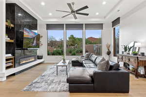 Living area with light wood-style flooring, a raised ceiling, a fireplace, a ceiling fan, and recessed lighting