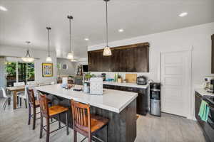 Kitchen featuring light countertops, pendant lighting, a breakfast bar area, dark brown cabinetry, and recessed lighting