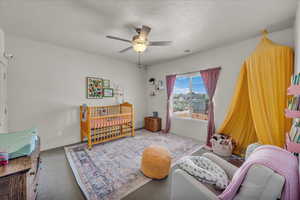 Carpeted bedroom with a crib, a textured ceiling, and a ceiling fan