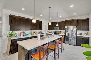 Kitchen with dark brown cabinetry, stainless steel appliances, pendant lighting, a kitchen bar, and recessed lighting