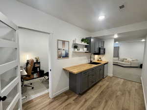 Kitchen featuring butcher block counters, light wood-style floors, gray cabinets, open shelves, and open floor plan