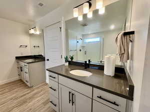 Full bath featuring two vanities, a shower stall, and light wood-type flooring